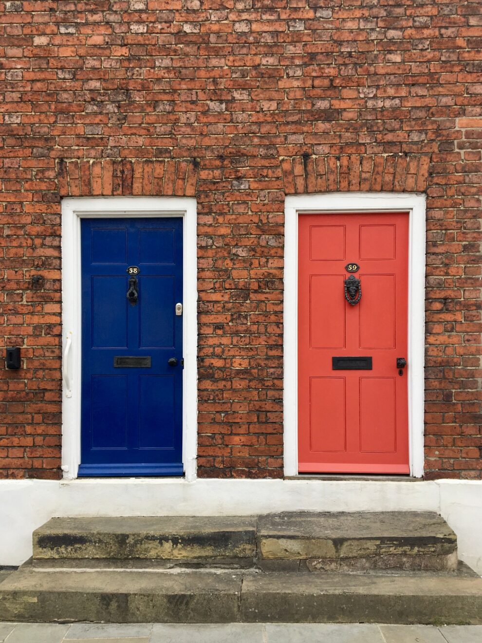 Two front doors side by side, one blue and one red, representing the choice to sell first or buy first before a move